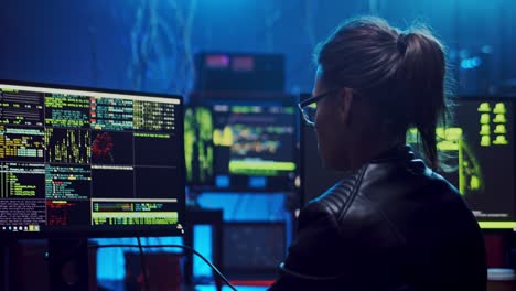 rear of the close up of the female software developer in glasses working and hacking programs or codes at the big screen of computer at night