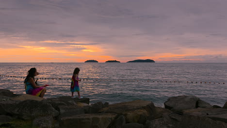 korean mother with little mixed girl at rocky sunset island beach in kota kinabalu - wide