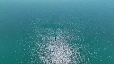 birdseye view of lone boat drifting in open ocean on glistening water