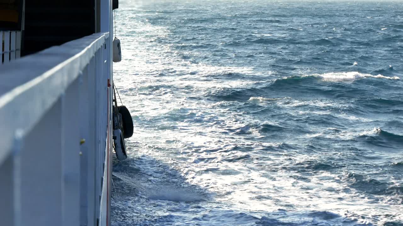 Schaumige Wellen, die hinter dem Heck einer Fähre auf dem blauen Wasser des Ionischen Meeres aufsteigen