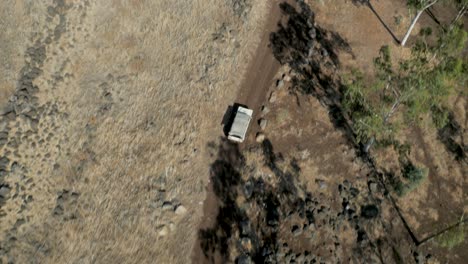 aerial tracking off-road car driving along winding dirt road in arid bushland