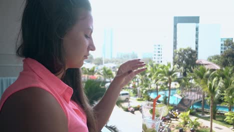 girl stands on hotel terrace and drinks sweet tasty mojito