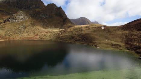 Vista-Aérea-Del-Lago-Azul-Profundo-Que-Refleja-La-Montaña-Con-Una-Enorme-Montaña-Detrás-Durante-El-Otoño-En-Suiza