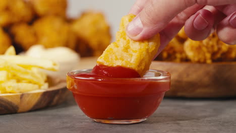 hand dipping chicken nuggets in ketchup
