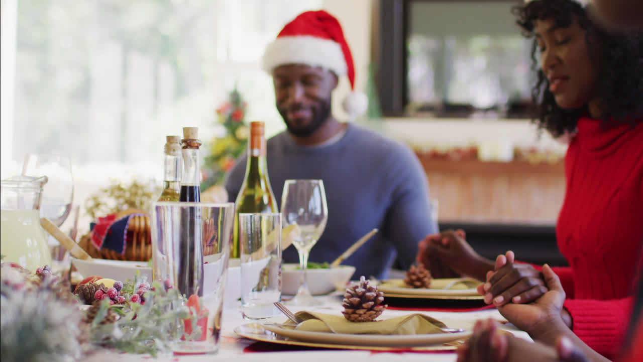 Afro-Amerikaans gezin met kerstmutsen, dat handen vasthoudt en bidt