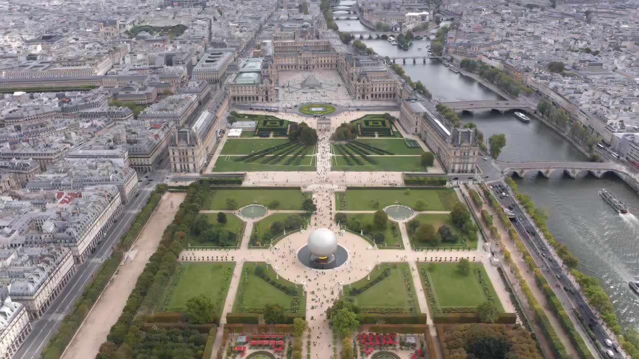 Aerial drone view rising over the Tuileries Garden capturing the Louvre with Pyramid, the Seine River, the Olympic Games cauldron ball and the historic city skyline stretching into the horizon
