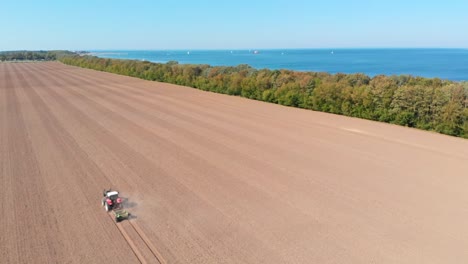 aéreo: tractor arando el campo junto al mar en el norte de alemania en un día soleado