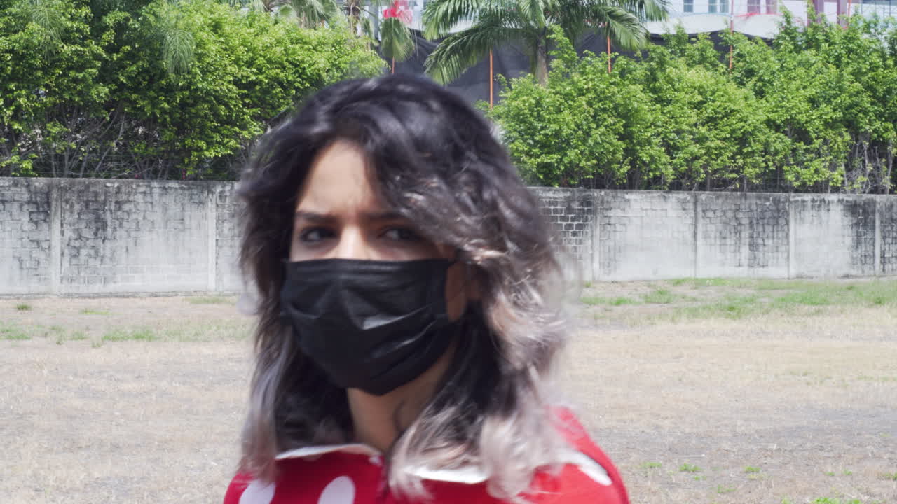 Unhappy stressed female walking outside wearing COVID protective mask, motion view