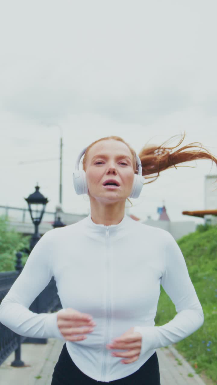 Energetic Woman Jogging in a White Athletic Top with Headphones on a Scenic Pathway, Capturing the Joy of Fitness and Outdoor Activities