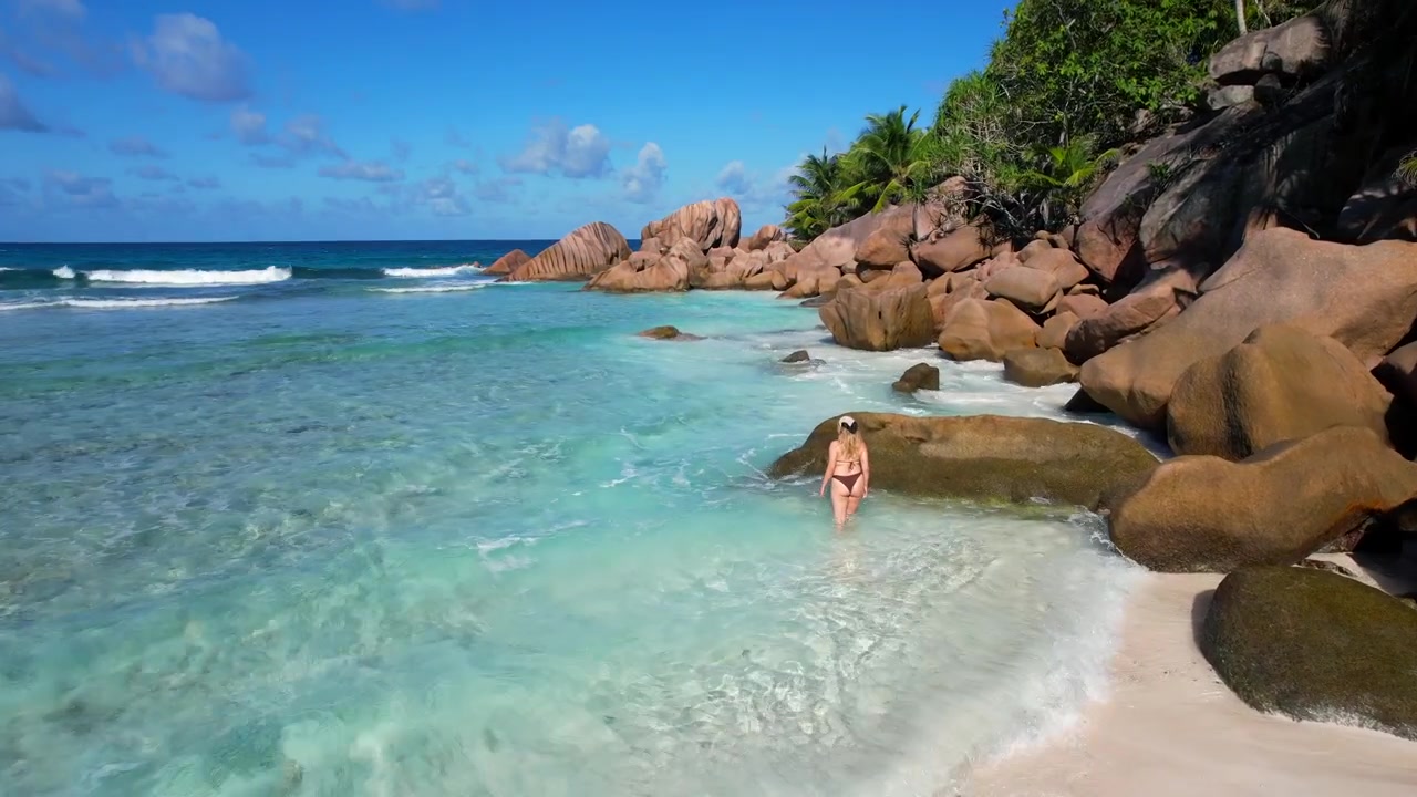 Viaggiatrice solitaria posa vicino all'acqua turchese su una spiaggia remota alle Seychelles. Ripresa aerea.