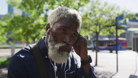 Close-up-of-african-american-senior-man-in-face-mask-wearing-earphones-on-the-road