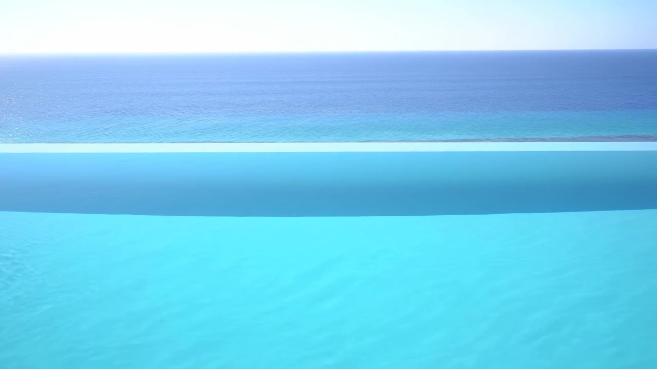 穏やかなさざ波が立つ透明なターコイズ色のプール水面を低く見渡し、細い縁とヤシの葉が穏やかな紺碧の海の地平線を縁取っている。広々とした空間と日差しが、穏やかなトロピカルリゾートの雰囲気を醸し出す。