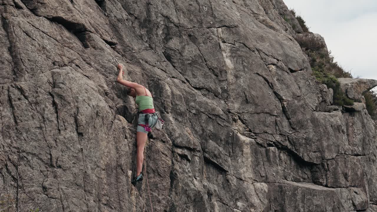 mujer fuerte escalando pared rocosa, vista de atrás