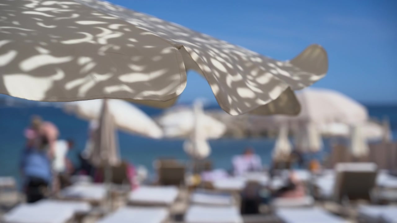Vista con effetto soft focus di un resort di lusso fronte mare, con file di lettini, ombrelloni decorativi e vista sul mare scintillante.
