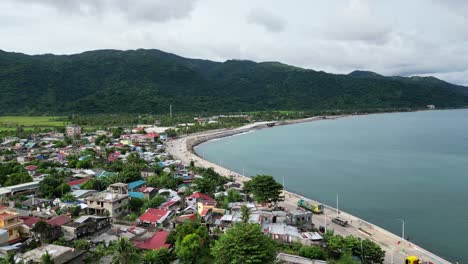 Breathtaking-aerial-footage-of-a-small-Philippine-village-on-an-island-near-the-ocean,-surrounded-by-forested-mountains