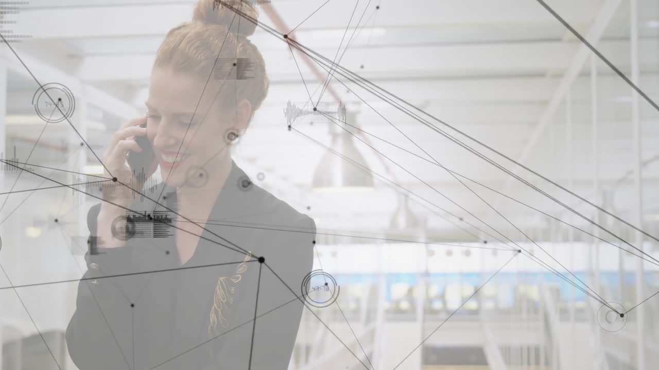 Woman talking on smartphone in technology office, showing network graphics and data charts