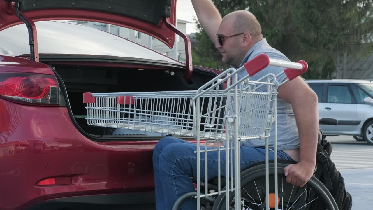 hombre adulto con discapacidad en silla de ruedas pone compras en el maletero de un coche en un estacionamiento de supermercado