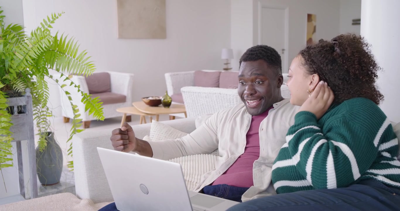 African American couple sitting on couch, man waving at laptop greeting caller, cuddling