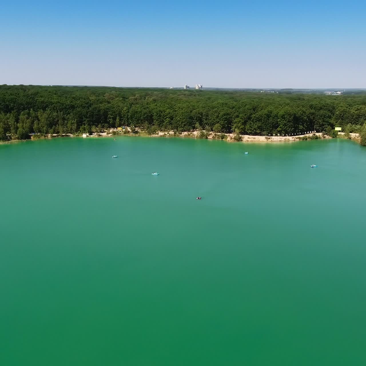 Smooth turquoise surface of water in former quarry. Drone footage over the lake and forest around it. Circle movement