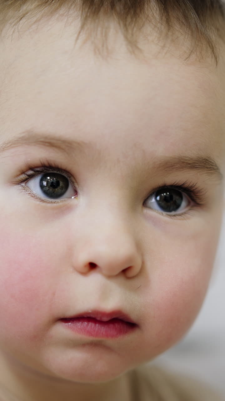 Angelic Caucasian baby boy looking at one point. Close up portrait of a calm cute kid. Vertical video