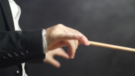 close up side view of conductor's hands holding a baton and moving quickly in the black studio