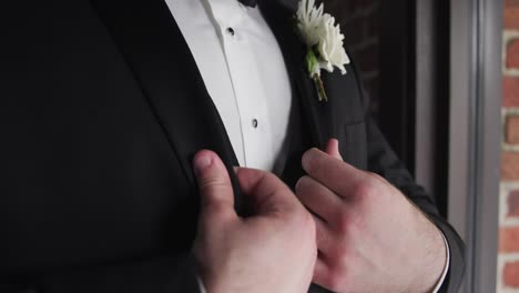 groom adjusting his suit with his hands on his wedding day in front of a window in slow motion