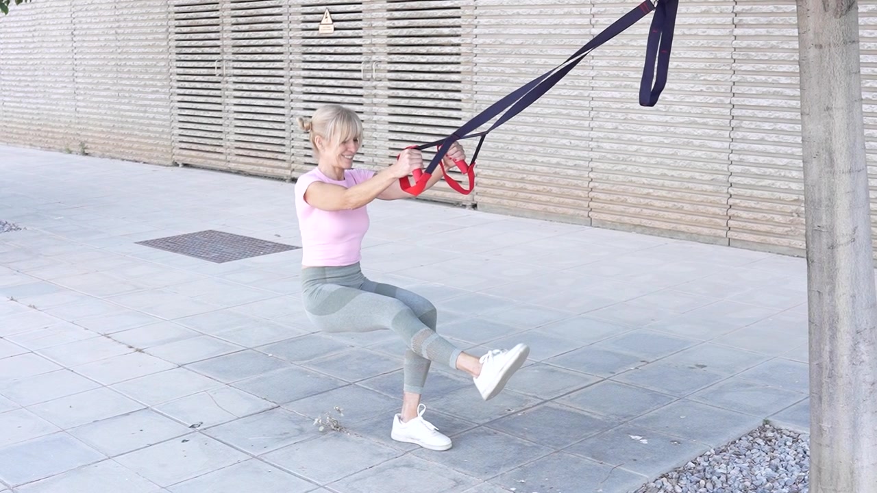 A woman is engaged in trx suspension training outdoors involving a full body workout