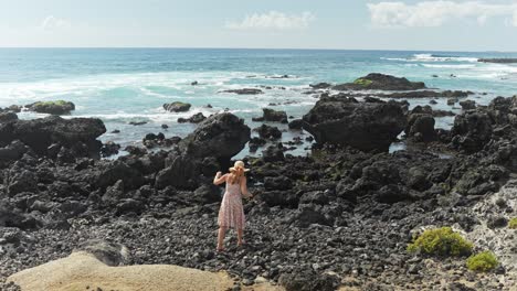 mujer caminando sobre rocas negras cerca de la orilla del mar mientras lleva un vestido floral, movimiento lento estático
