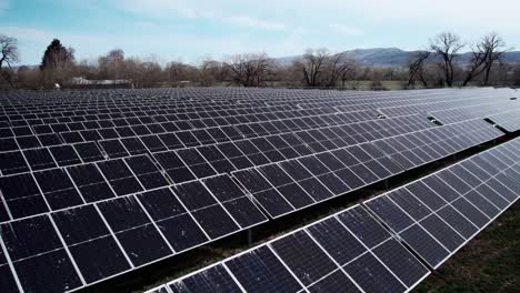 Slowly-passing-over-horizontal-rows-of-solar-panels-at-a-green-energy-farm,-aerial-dolly