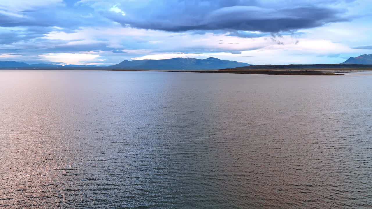 Vast waterscape with the silhouette of a mountain range at backdrop under the dramatic cloudscape. Iceland nature from top.