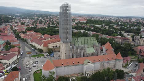 aerial view circling the cathedral of zagreb with scaffolding restoration on the upper tower overlooking croatian cityscape