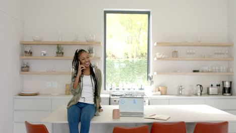 african american young woman talking on phone, sitting in kitchen