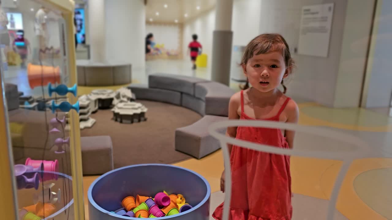 Female Toddler Pulling Pairs Of Colorful Sticky Suction Rubber Toys From Glass Surface In Indoor Playground