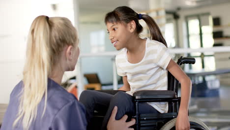 in rehabilitation center, assisting girl with cerebral palsy in wheelchair, therapist smiling