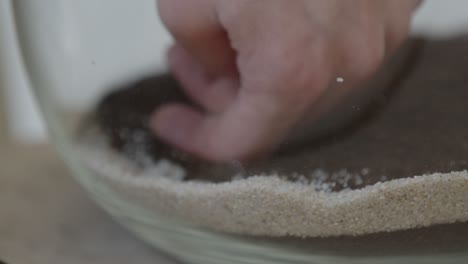 a young female botanist creates a tiny live forest ecosystem in a huge glass jar - putting the white sand - a tight close-up