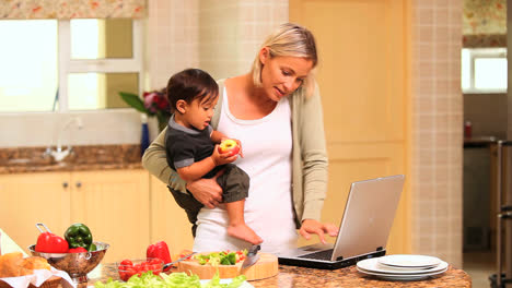 mother holding baby while working on laptop