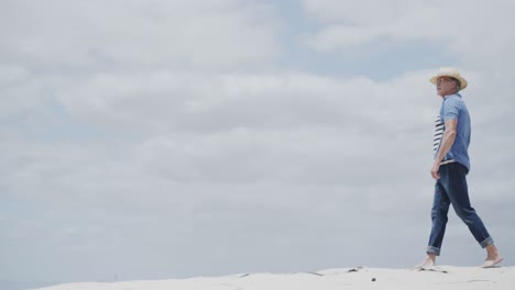 Happy-senior-caucasian-man-walking-barefoot-on-tropical-beach,-in-slow-motion