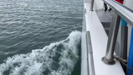 white boat sailing on ocean water causing a wake, view from side of boat