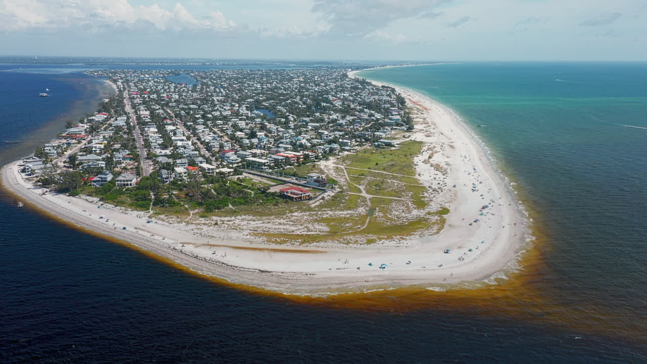 A sweeping aerial captures Anna Maria Island’s curved shoreline with soft sandy beaches, turquoise ocean waters, and a bustling seaside town framed by natural coastline