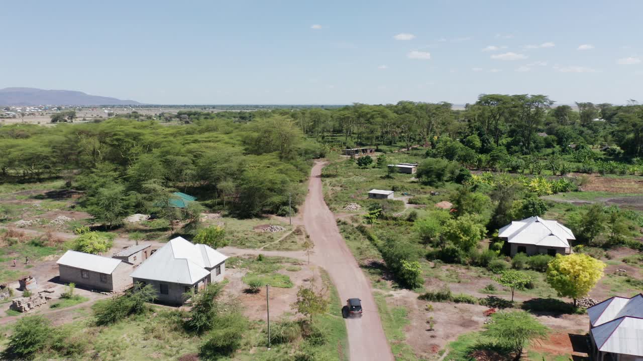 Aerial drone shot flying forward following a van driving in a little village next to Lake Manyara, Tanzania. Clear blue sky