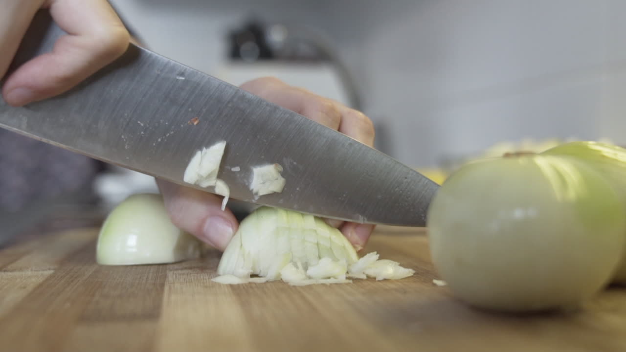 Slow-motion close shot as cutting, chopping an onion in the kitchen with a huge knife
