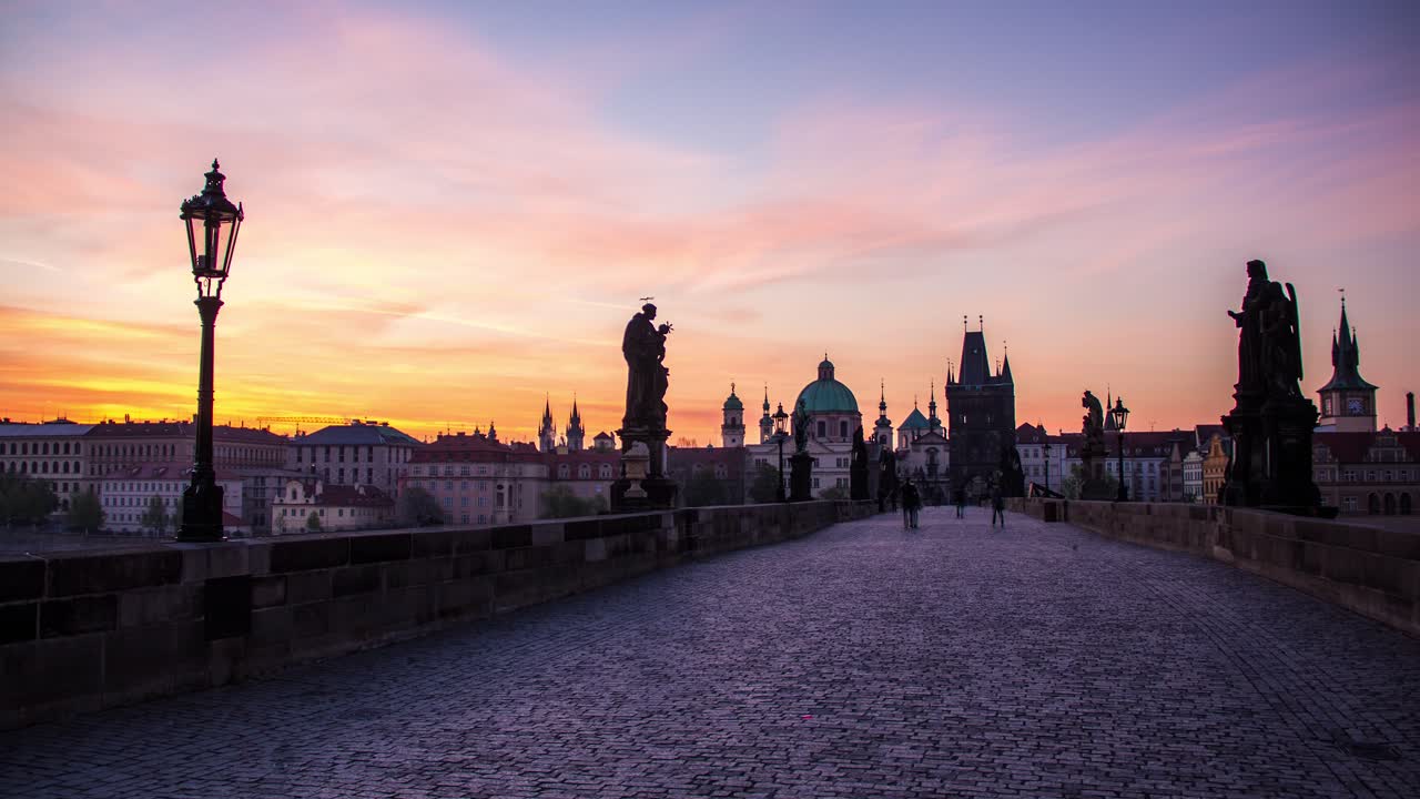 Timelapse del amanecer que va de la noche al día del Puente de Carlos en Praga, República Checa, con vistas al Casco Antiguo, estatuas, farolas y los adoquines del puente, mientras el cielo azul se tiñe de un dorado vibrante.