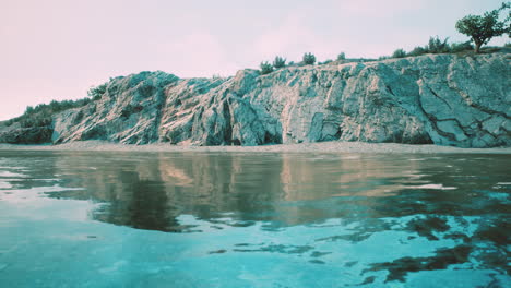 a serene river flowing past a rocky cliff with a reflection of the sky and trees in the water