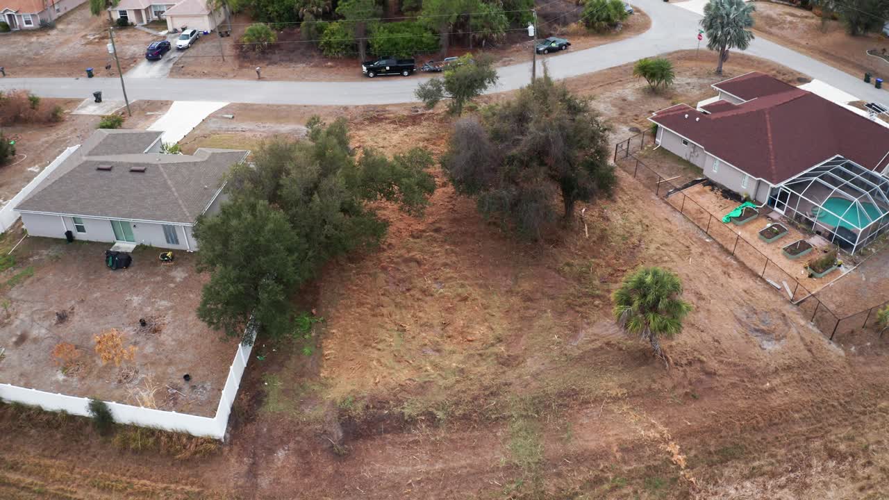 Um terreno baldio, delimitado por casas, está sendo preparado para desenvolvimento. A área apresenta vegetação esparsa e propriedades residenciais próximas. Útil para imagens de imóveis ou planejamento urbano.