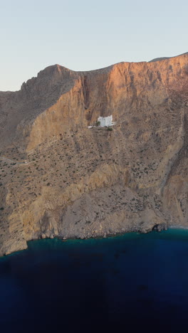 holy monastery of the virgin mary chozoviotissa, the panagia hozoviotissa monastery on steep cliff above aegean sea at sunrise, amorgos island, aerial vertical shot