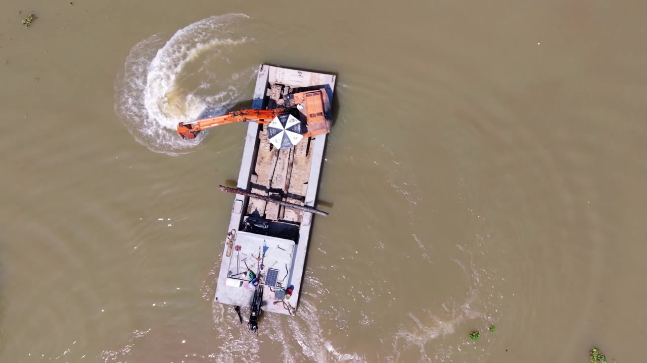 Ripresa dall'alto di un escavatore che smuove l'acqua fangosa del fiume Mekong durante il giorno. Prospettiva aerea che cattura un operatore asiatico su una draga che lavora nel fiume Mekong durante le ore diurne.