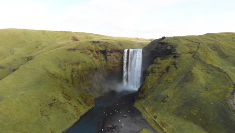 Rugiente-Cascada-De-Skogafoss-En-Islandia-Con-Turistas-Admirándola-Debajo