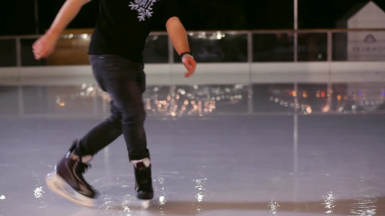 Ice skating boy performs an ice-skating fancy footwork. Only his feet are in shot. Camera is following his movement. It is a nighttime. Footage in HDs