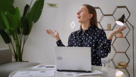 a successful young woman using a laptop, sitting on a chair, earning money, dollar bills falling from above