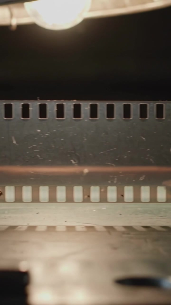 Video verticale: Accensione di una lampada che rivela una pellicola cinematografica su un tavolo con una lente da riparare.